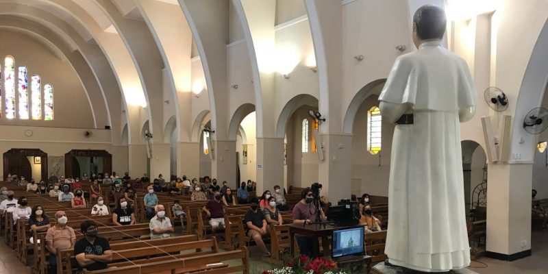 Devotos sentados de frente à imagem do Padre Eustáquio, mantendo o distanciamento social.