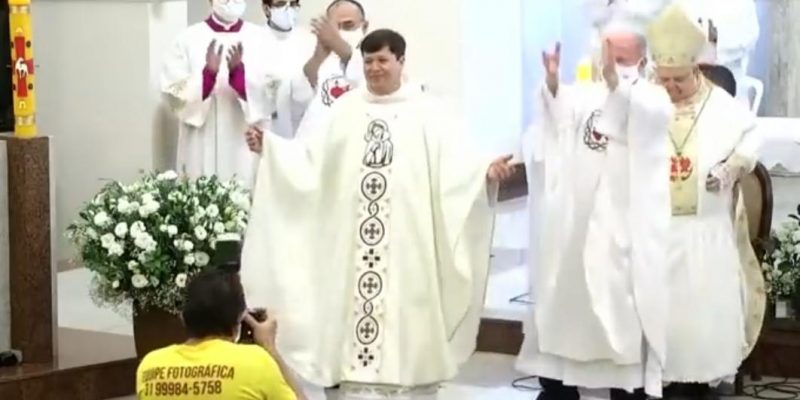 Padre armin, no altar da igreja do Padre Eustáquio, se apresentando para a comunidade como novo padre, durante sua ordenação. Sendo aplaudido e fotografado